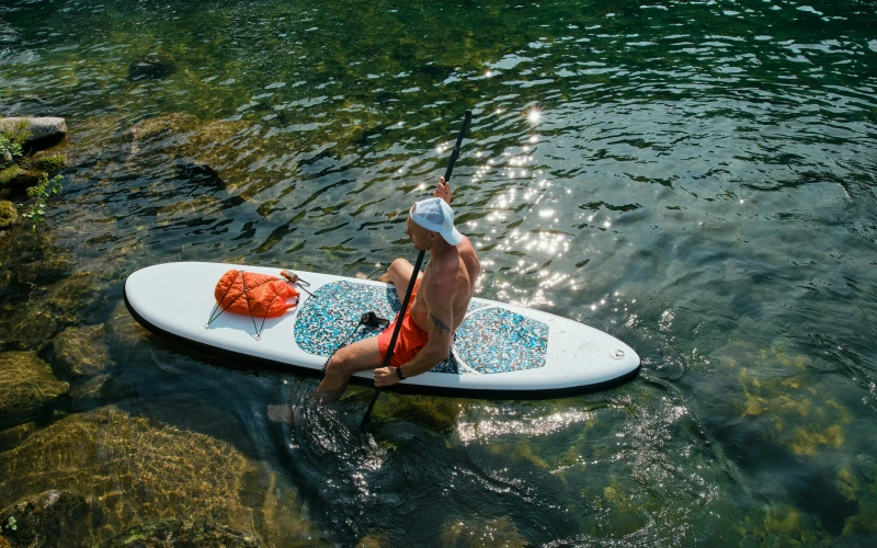 Man in bathing suit sitting on a paddle board with his feet in the water