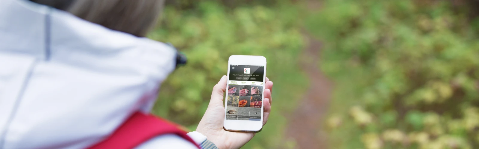 Woman in a hoodie holds up a phone with a trail into the woods ahead
