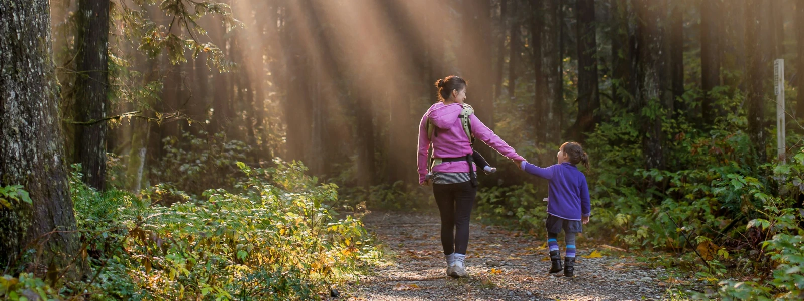 A mother and child walking towards a sunlit wooded area