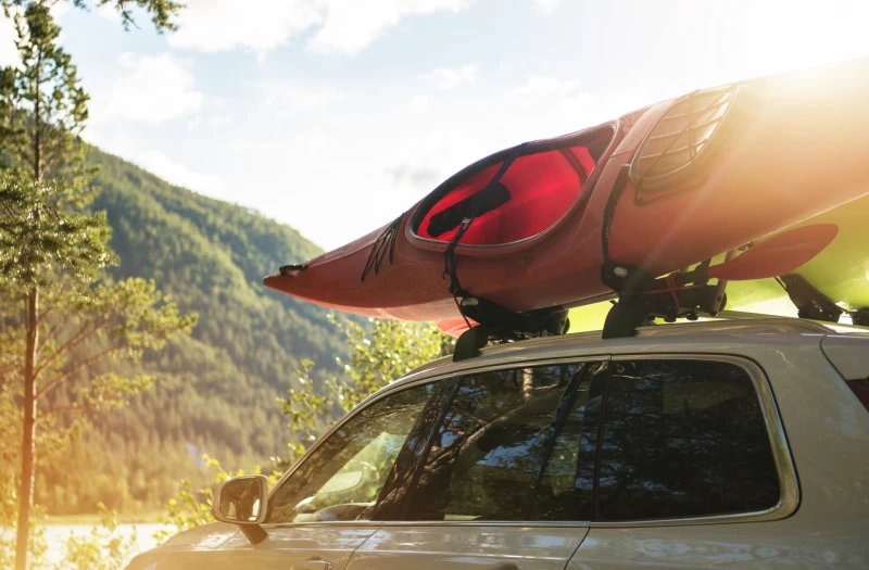 Car with kayak on roof beside a lake and mountains.