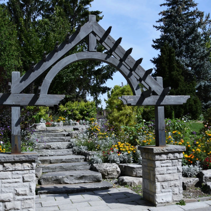 Outdoor wooden archway entry leading to stone stairs that are surrounded by flowers.