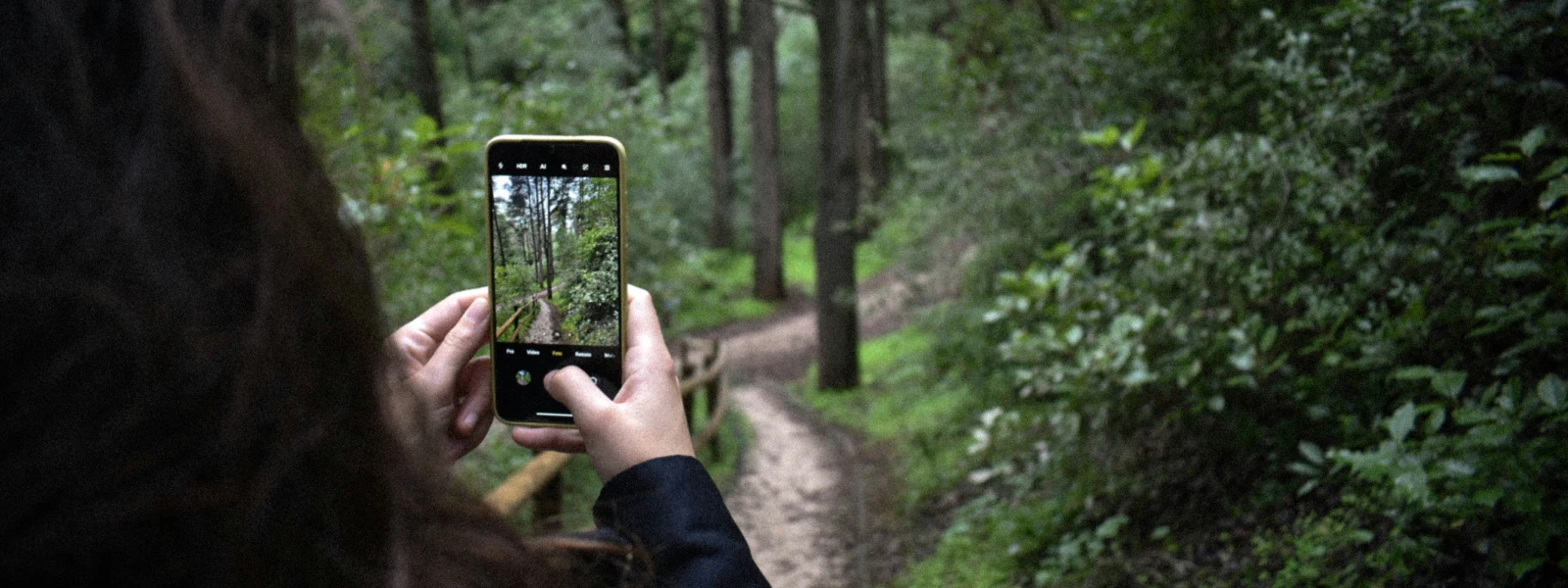 Woman taking a photo on her phone of the wooded trail ahead