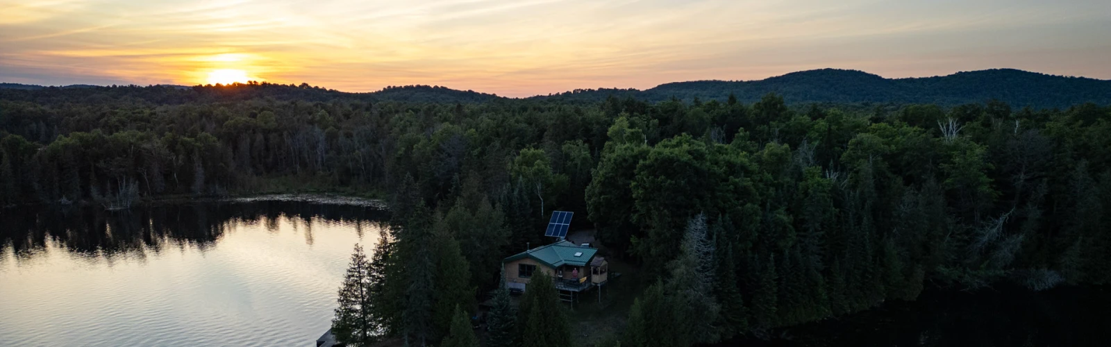 Lake front house surrounded by trees with the sun setting the distance
